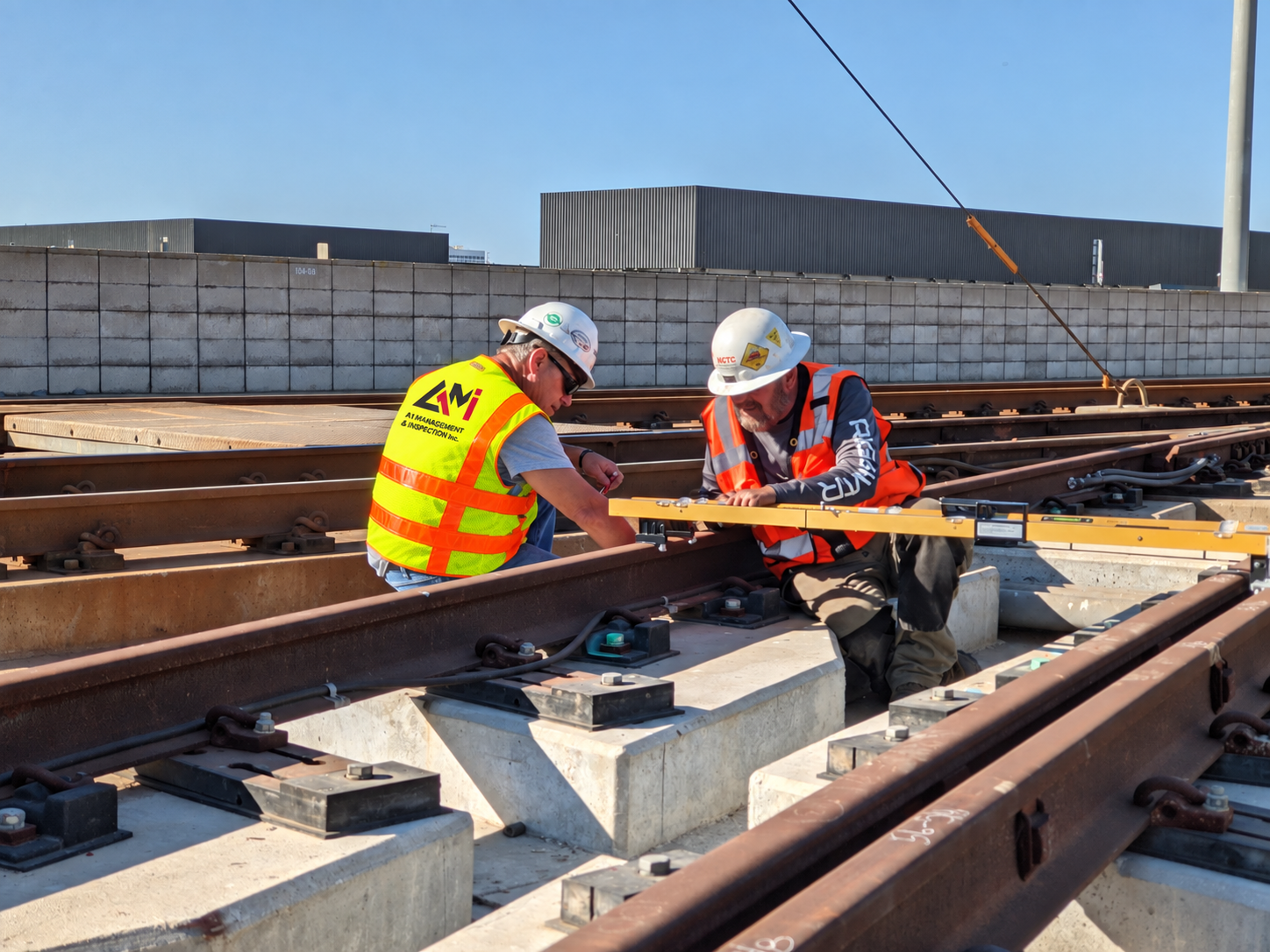 Two construction workers in safety vests and helmets inspecting railway tracks on an outdoor construction site.