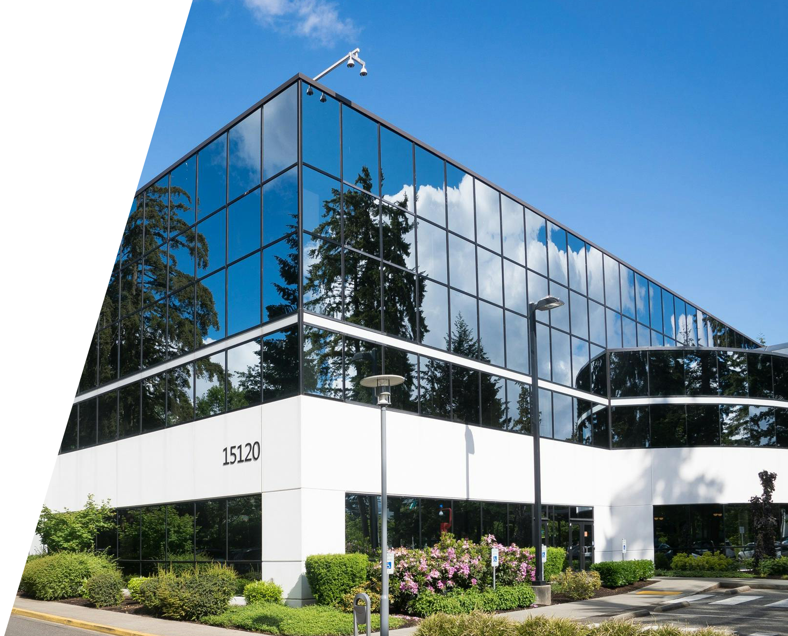 Modern glass office building exterior reflecting trees and sky, representing business insurance for small companies and corporate offices.