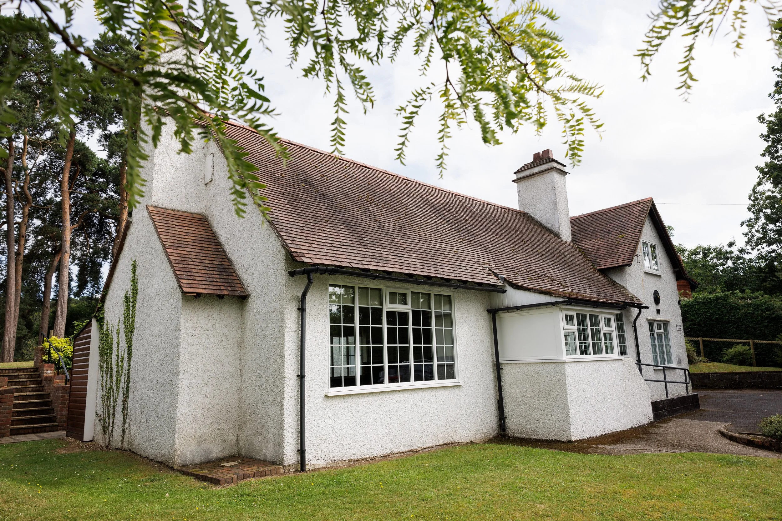 The Sands Room with a pitched roof, large front window, and a small porch with a black railing, surrounded by green grass and trees.