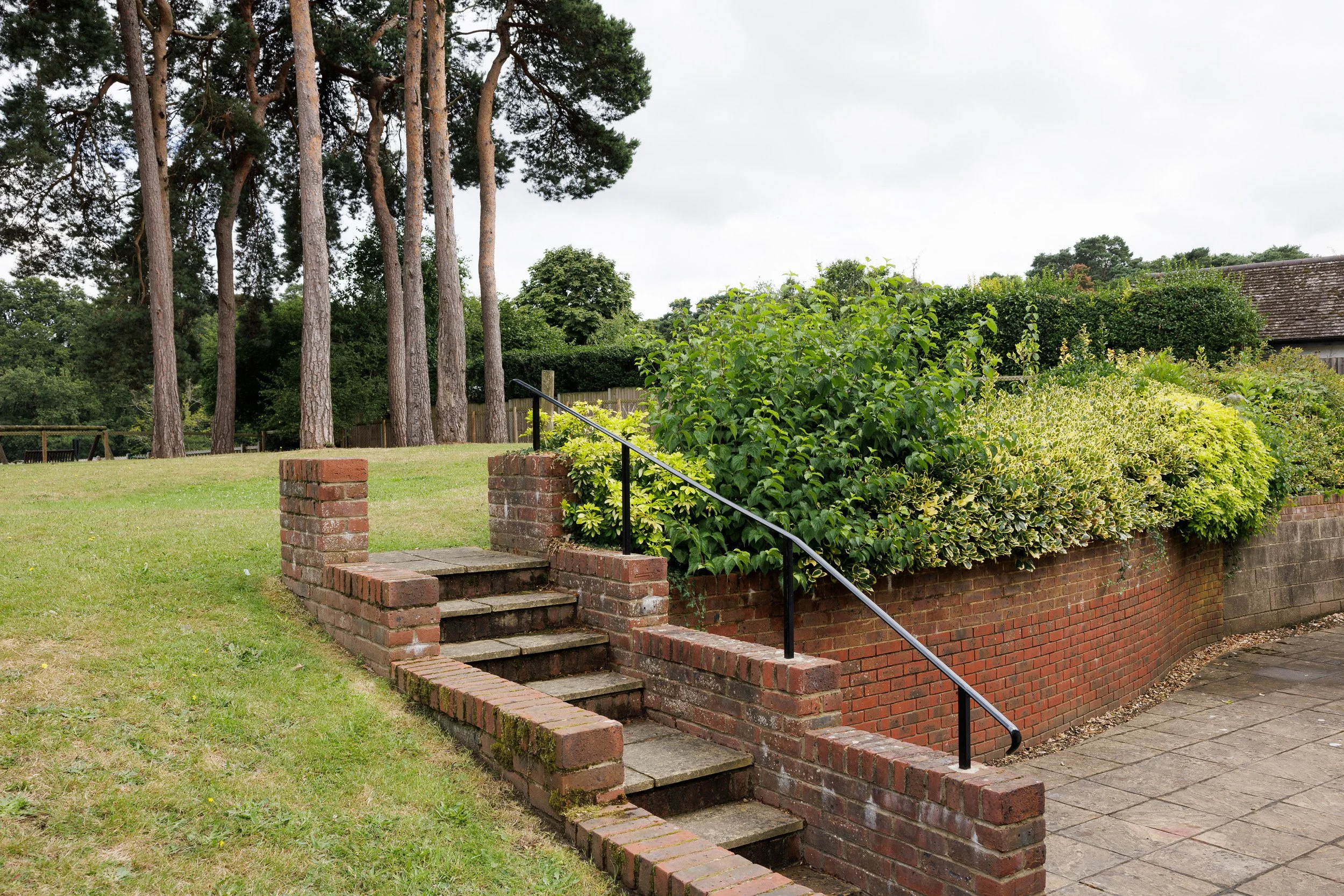Outdoor scene with brick stairs, green shrubs, trees, and a cloudy sky.