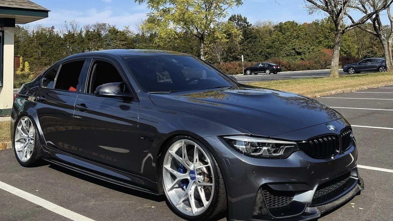 A black BMW sedan parked in a parking lot with trees and other cars in the background.