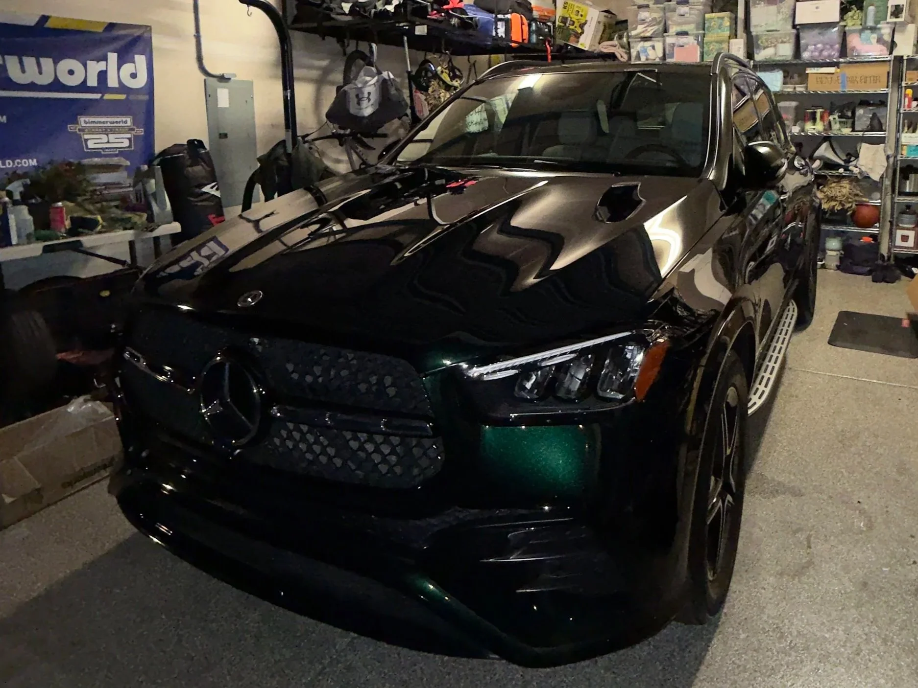 A black Mercedes-Benz car parked in a garage filled with various items and shelves.