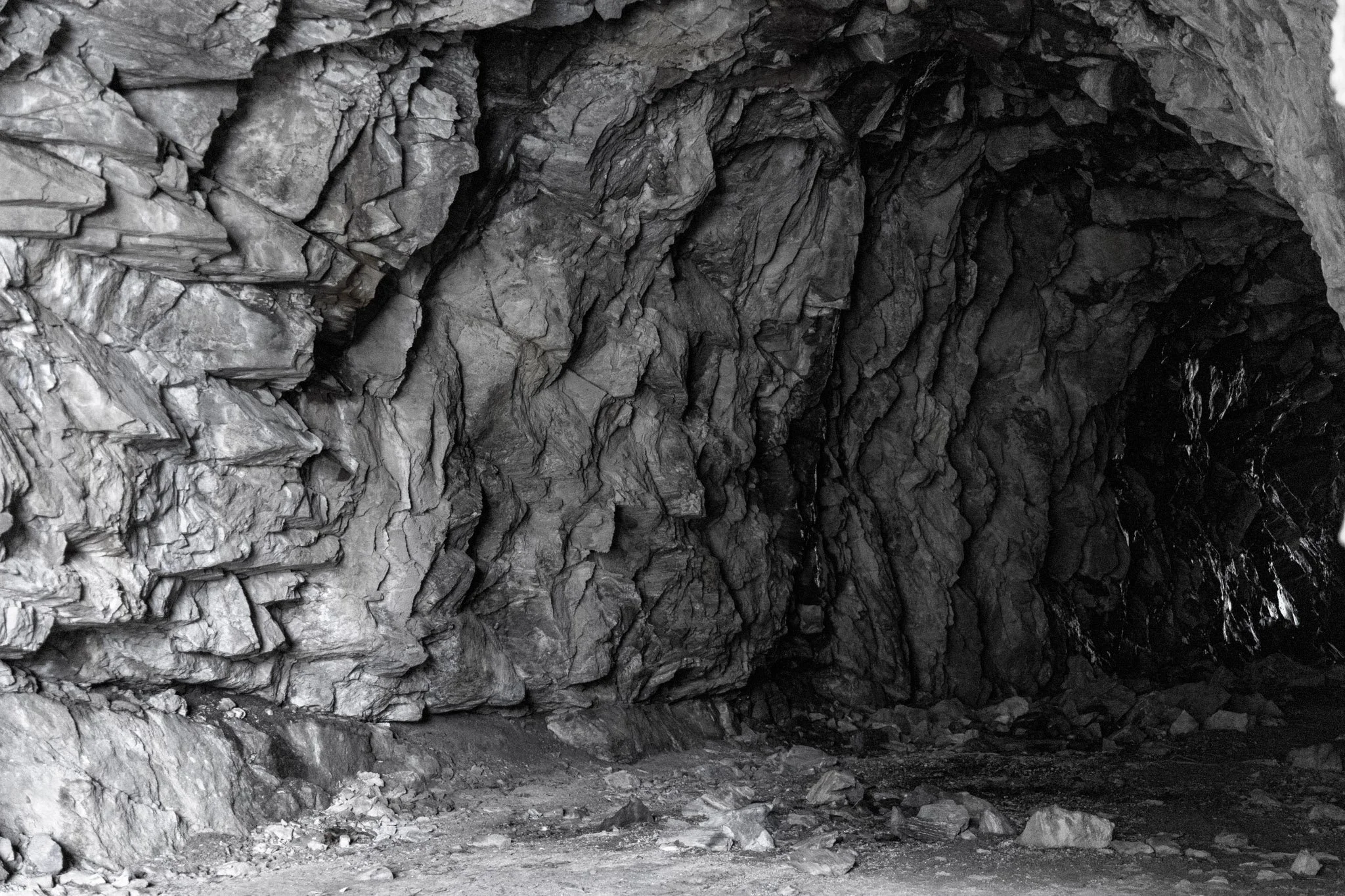 A black and white photo of a rocky tunnel or cave with jagged rock formations on the walls and ceiling.