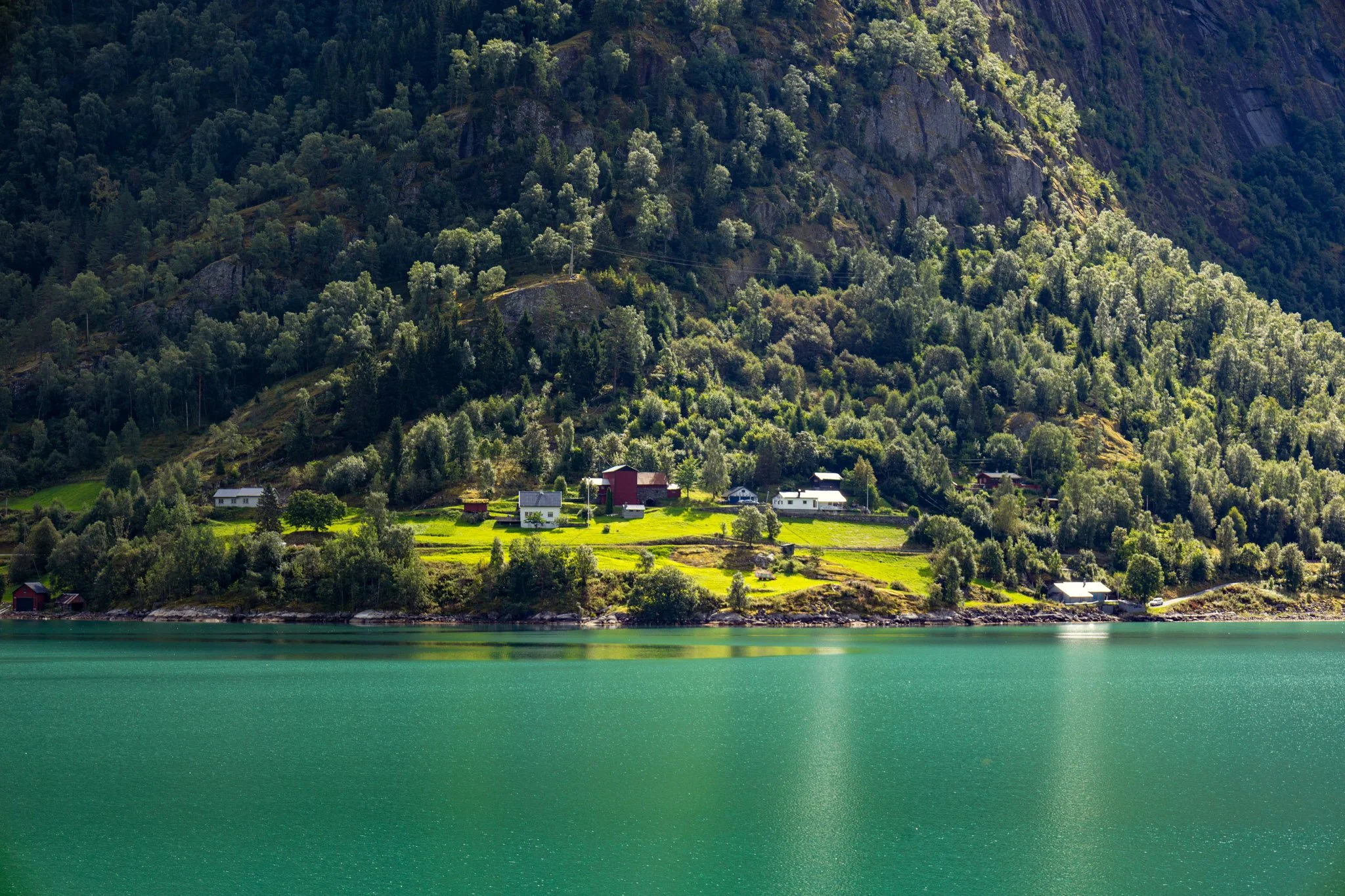Scenic view of a mountain landscape with lush green trees and houses near a vibrant green body of water.
