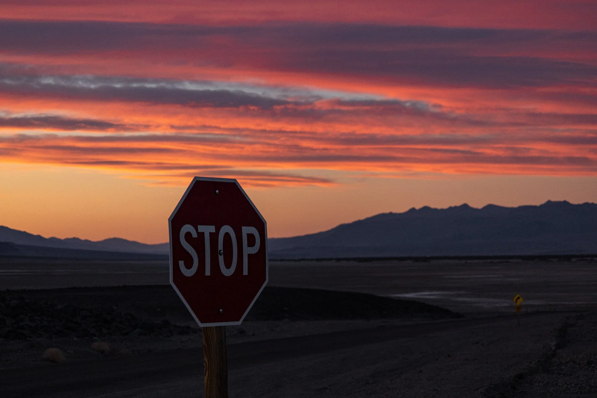 A stop sign in foreground with a colorful sunset sky in the background and mountains in the distance in Death Valley.