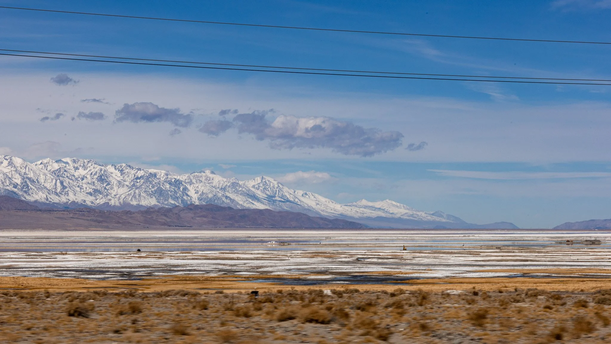 Snow-capped mountains under a partly cloudy sky with power lines in the foreground.