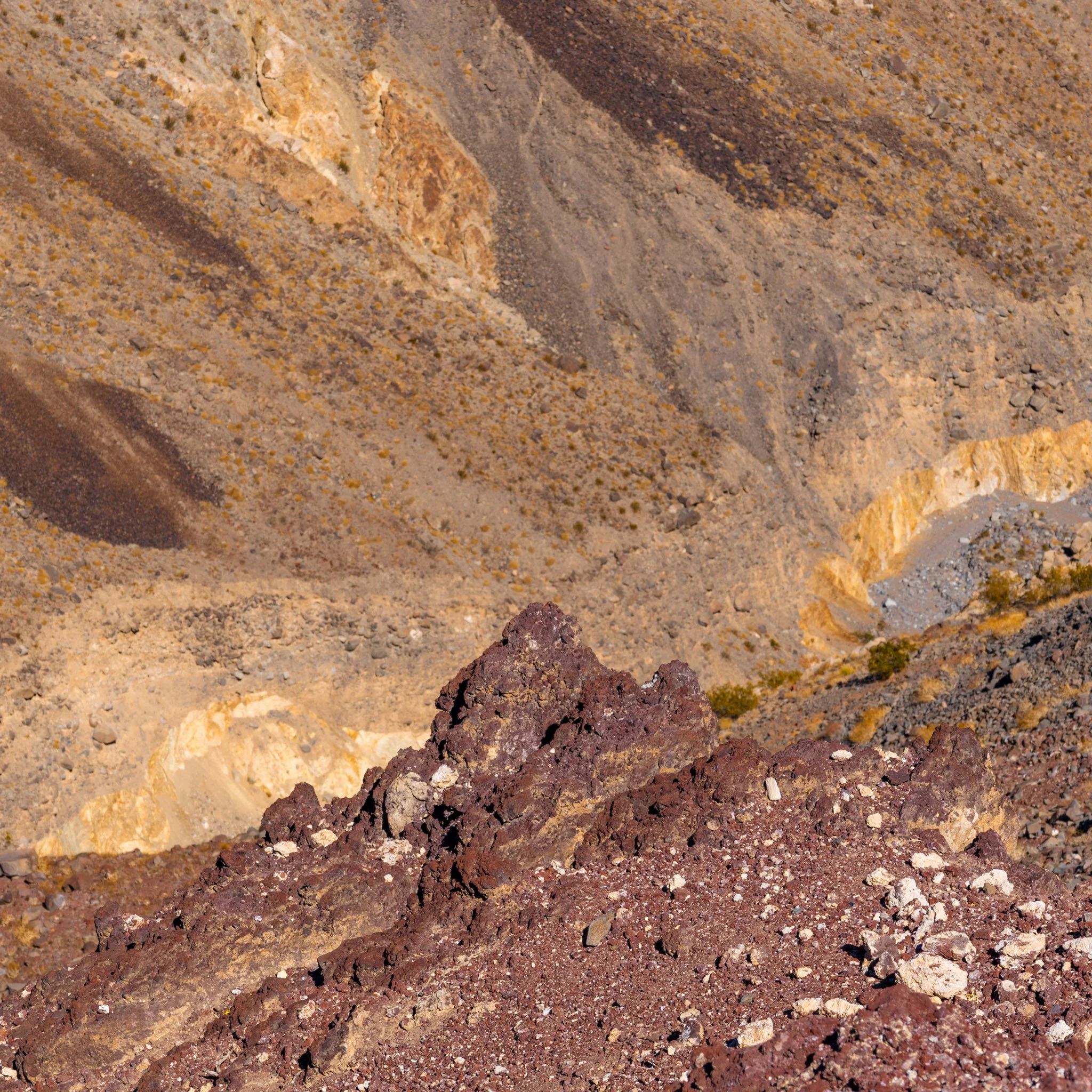 Close-up view of volcanic rocks with various colors including brown, red, yellow, and beige, arranged in layers with some small pebbles and gravel at the bottom.