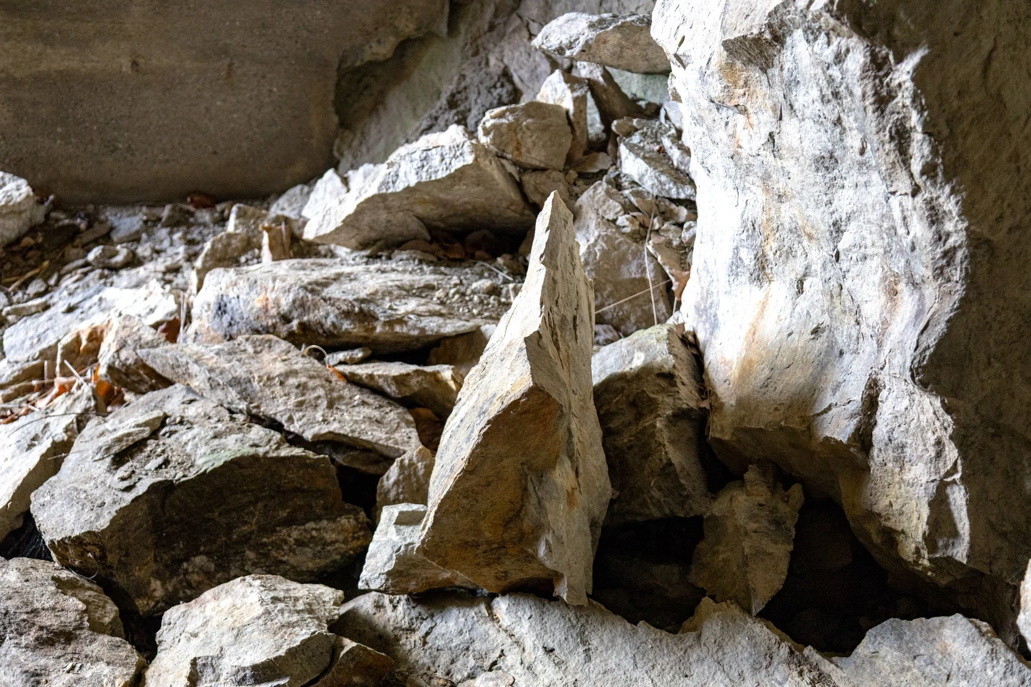 Close-up view of a small pile of light-colored, rough-textured rocks in a dark, rocky environment.