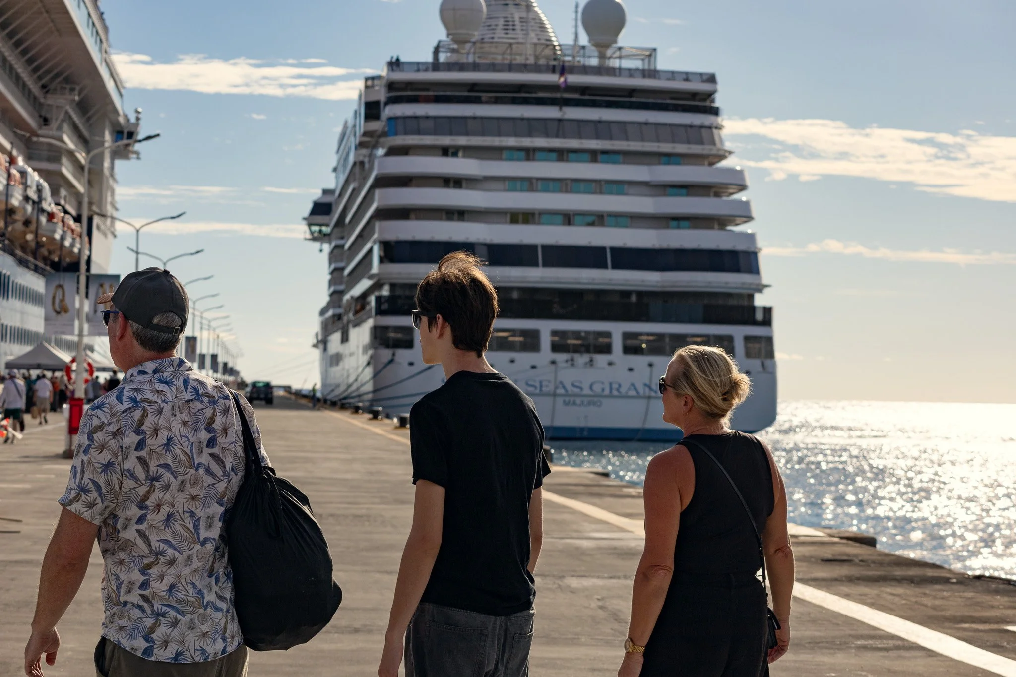 Four people walking along a harbor with a large cruise ship docked nearby in the background.