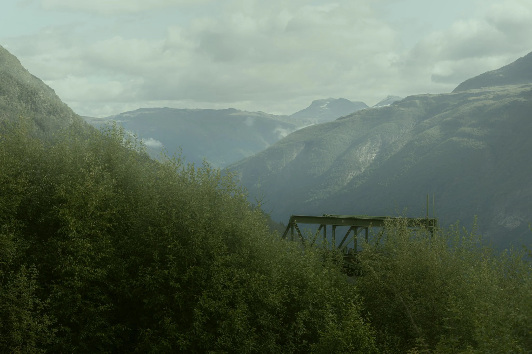 Scenic view of green, forested mountains under a cloudy sky with a small wooden structure in the foreground.