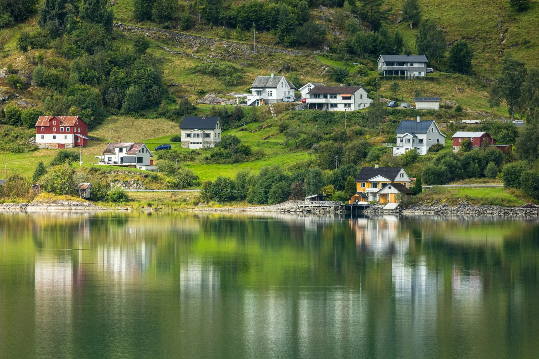 Houses on a hillside by a body of water, reflection of the houses and trees in the water