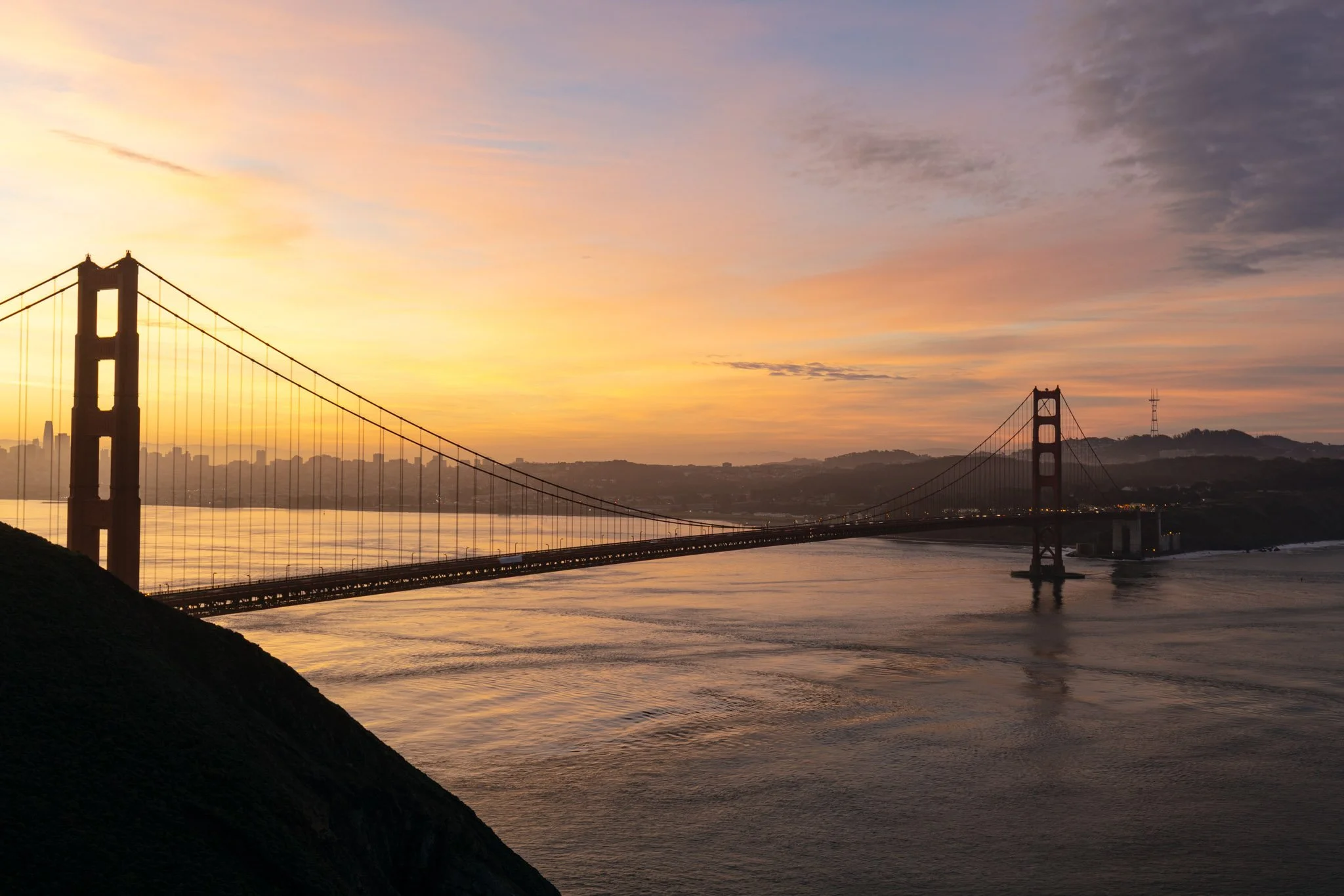Sunset over the Golden Gate Bridge in San Francisco, with a colorful sky and calm water below.