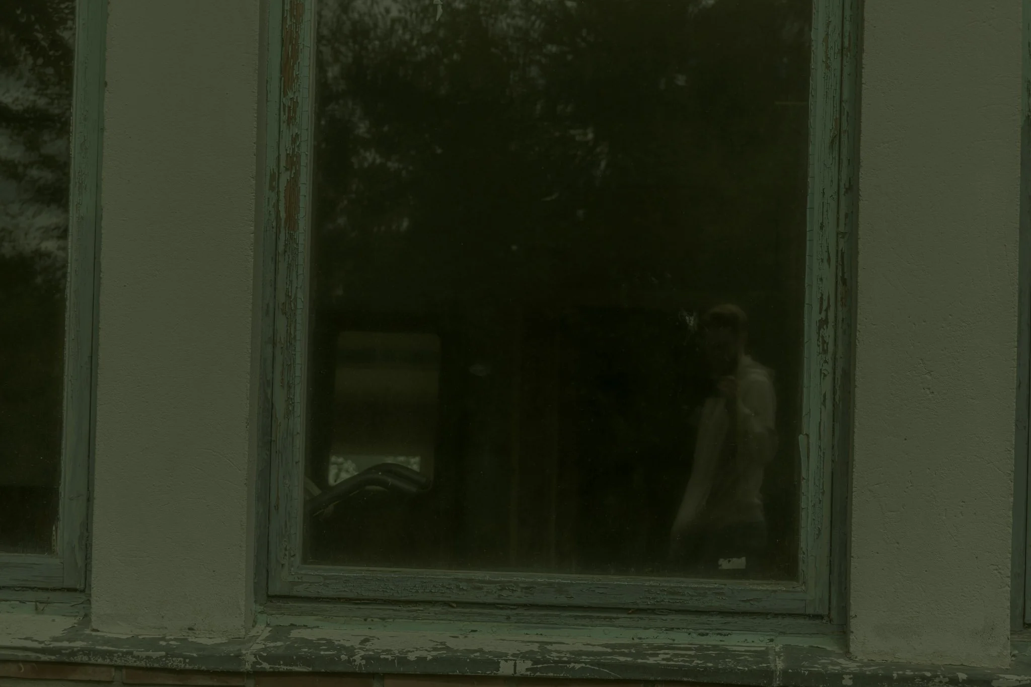 A window with peeling blue paint on the frame, set into a beige wall with visible texture.
