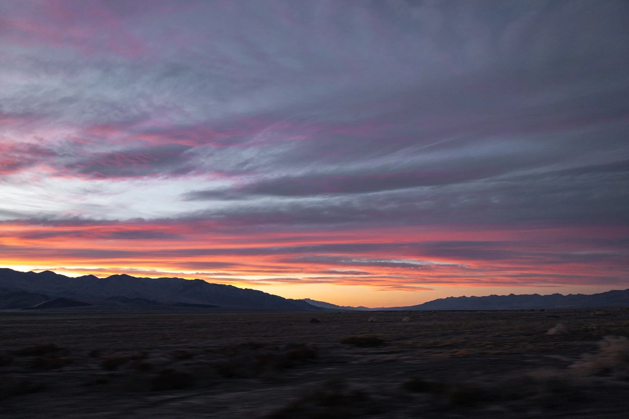 A sunset over mountains with colorful clouds in the sky in Death Valley, showing shades of pink, purple, and orange.