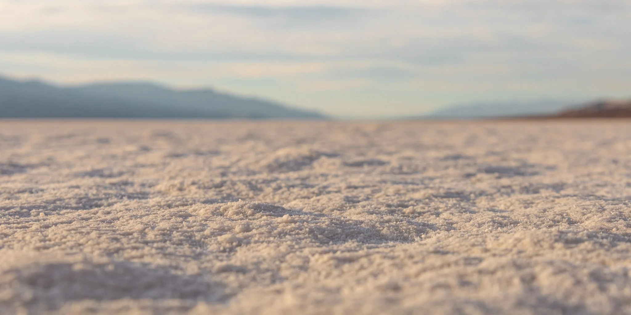 Close-up view of a salt flat with textured crystalline salt surface extending to distant mountains under a partly cloudy sky.
