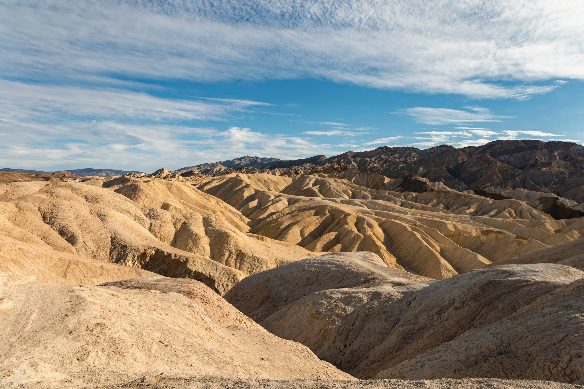 Desert landscape with beige, rocky, and ridged terrain under a partly cloudy sky with white and gray clouds.