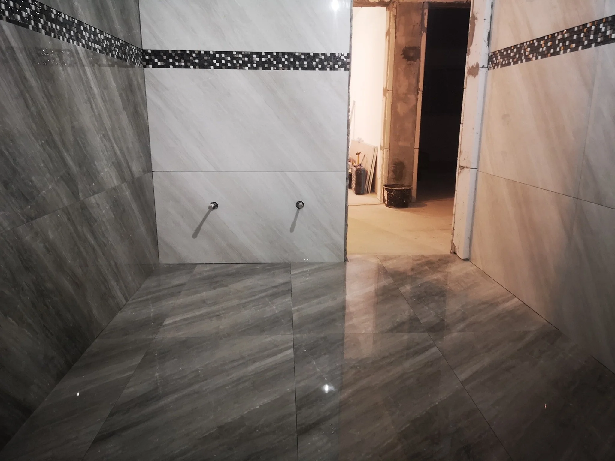 A partly finished bathroom with tiles on the walls and floor, with some tools, buckets, and construction materials visible in the background.