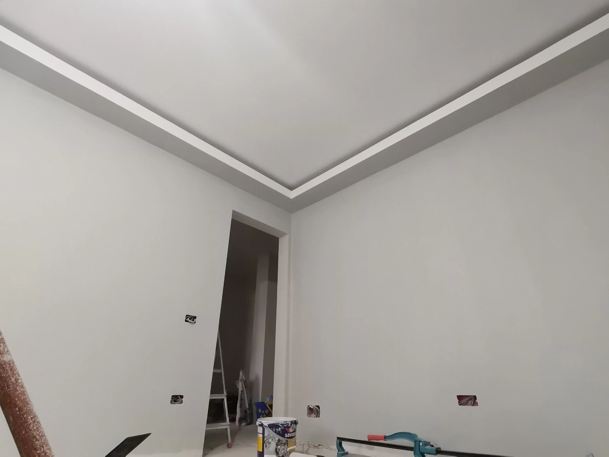Interior room with unfinished ceiling, visible wiring, and construction tools, including a ladder, paint cans, and a toolbox.