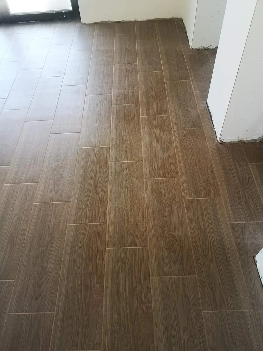 Wood-like tile flooring in a room with a door and white walls.