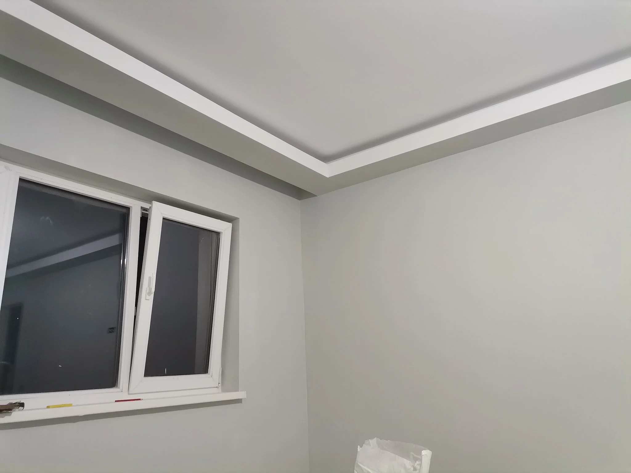 An open window with a white frame in a white room with gray walls and a white ceiling with layered crown molding.