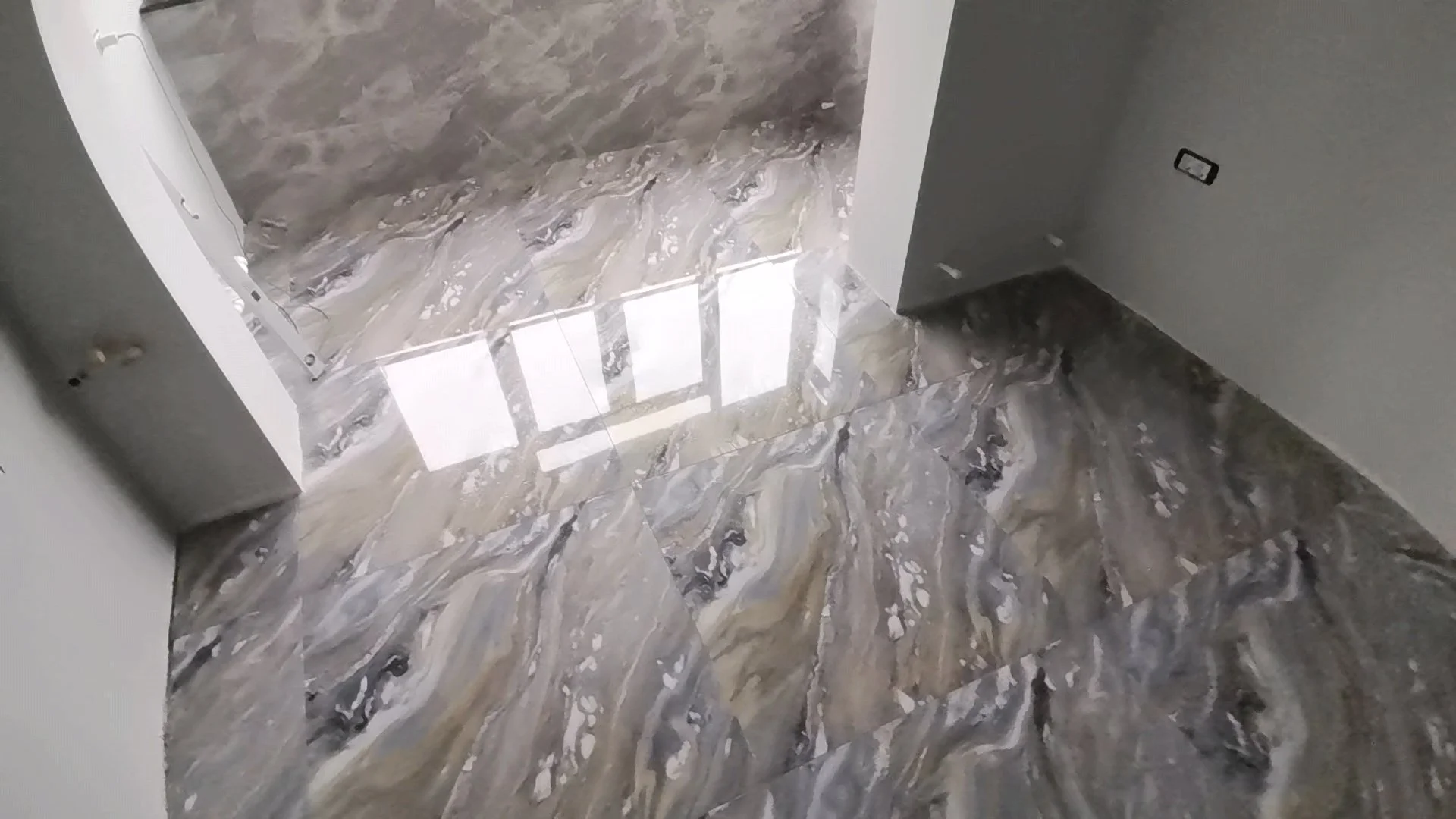 Room with marble flooring and marble wall, with an open doorway to another room. Electrical outlets are visible.