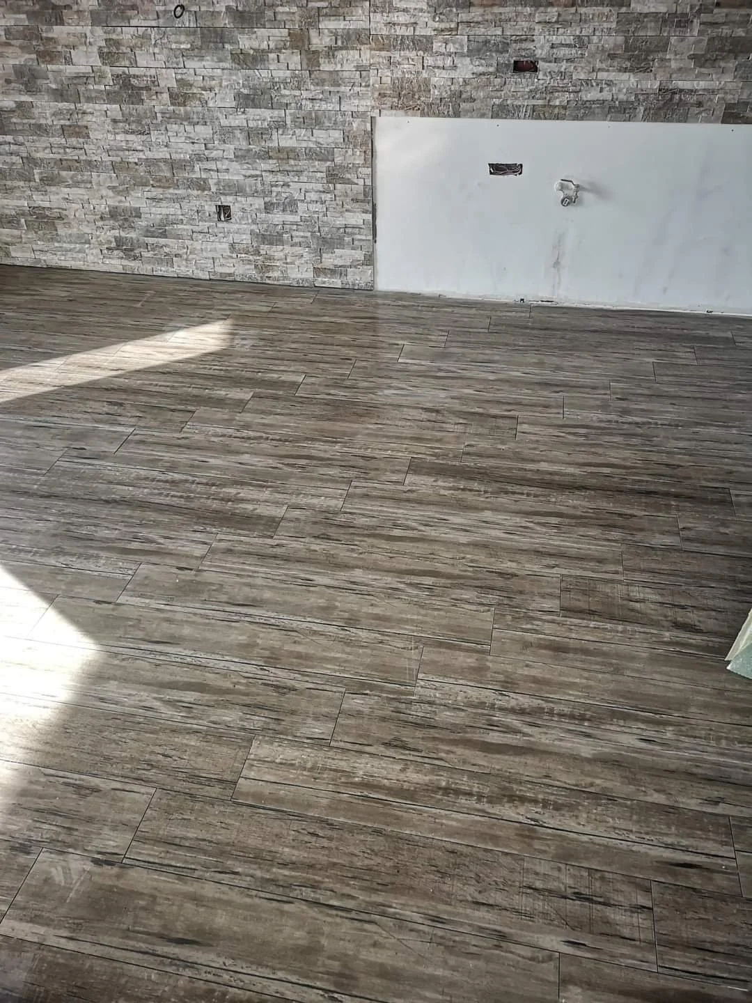 Interior space with wood-look tile flooring, stone accent wall, and an unfinished wall with electrical fixtures and outlets.