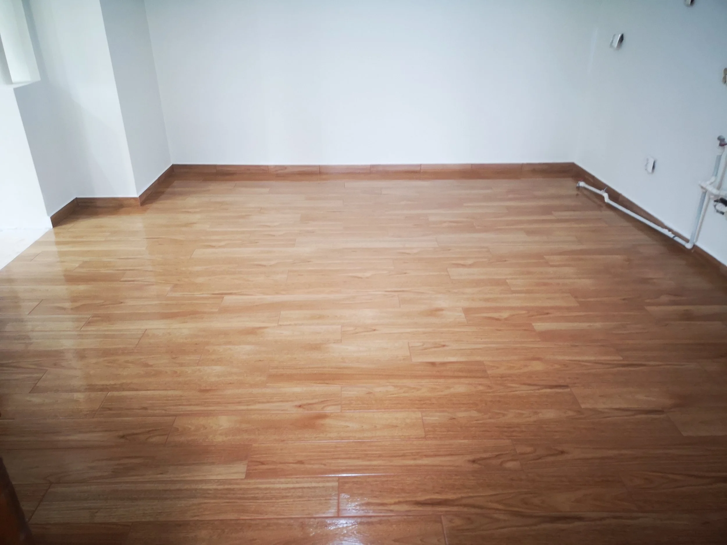 Empty room with light-colored hardwood flooring, white walls, and pipes along one wall.