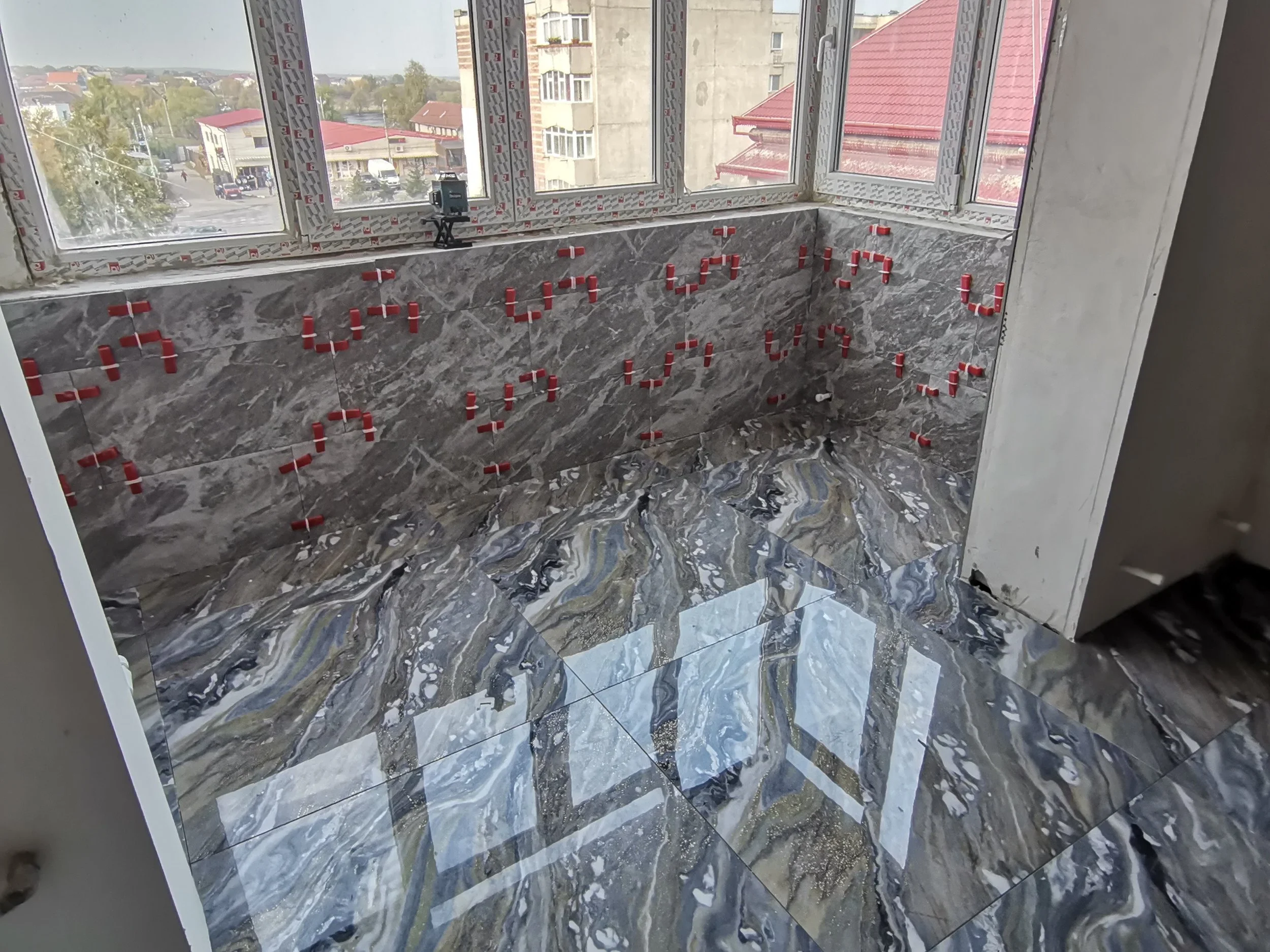 Interior of a room under construction with marble tiled walls and floor, and red spacers arranged on the walls forming the word 'LOVE'.