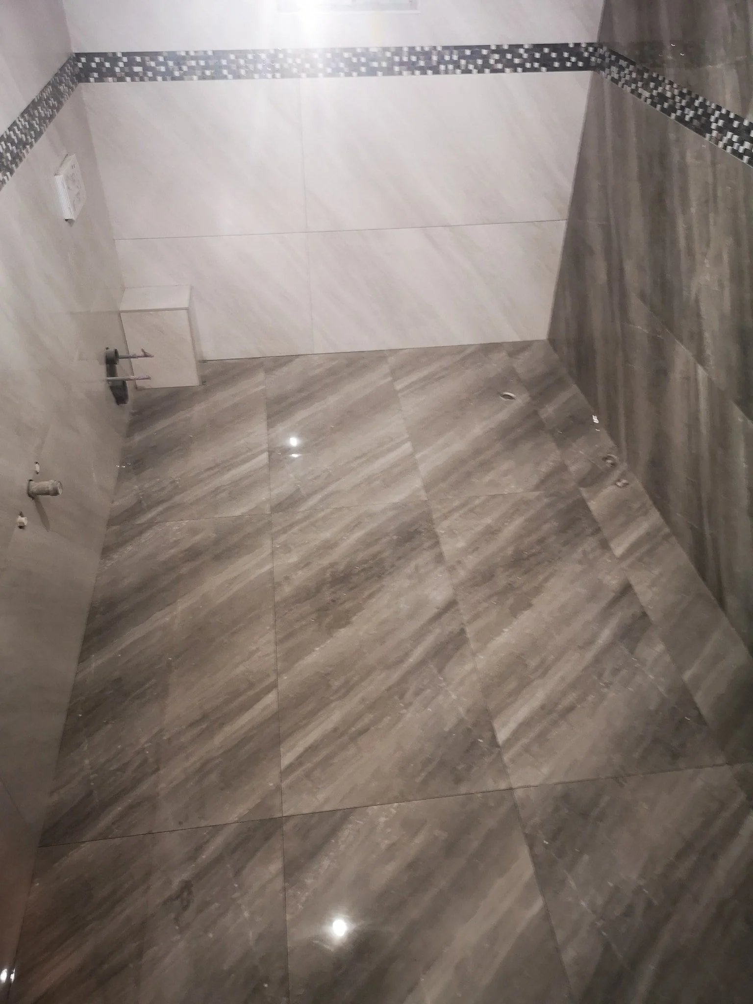 Empty bathroom with gray and white tiled walls and gray tiled floor, with plumbing fixtures absent.