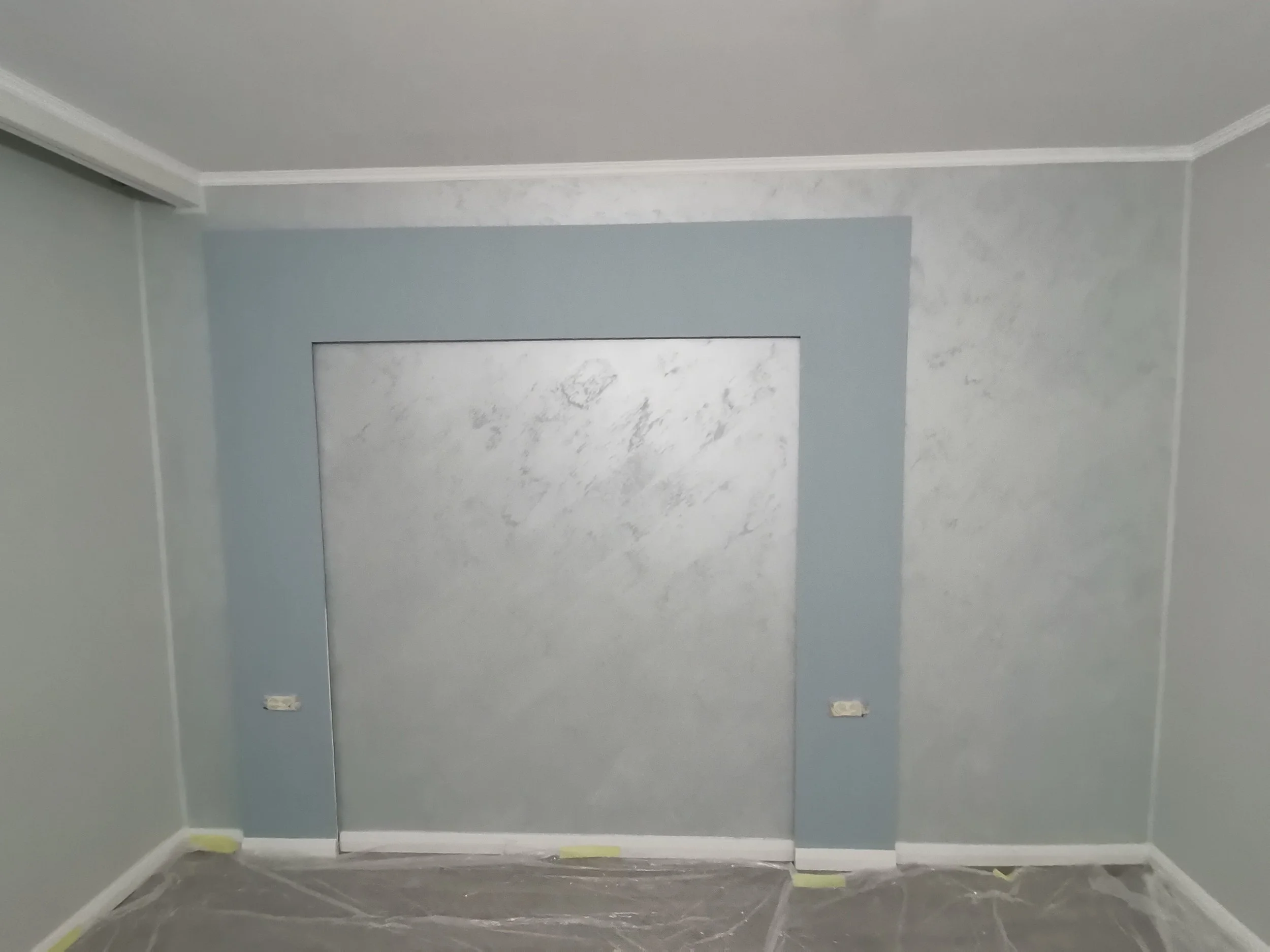 Room under renovation with blue walls, white ceiling with crown molding, two electrical outlets, and taped floor.