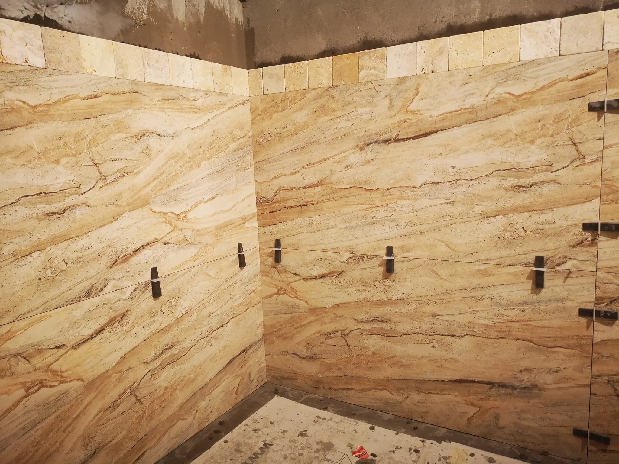 Interior corner of a room with beige and brown marble tiles on the walls, some black clips and a small piece of trash on the floor.