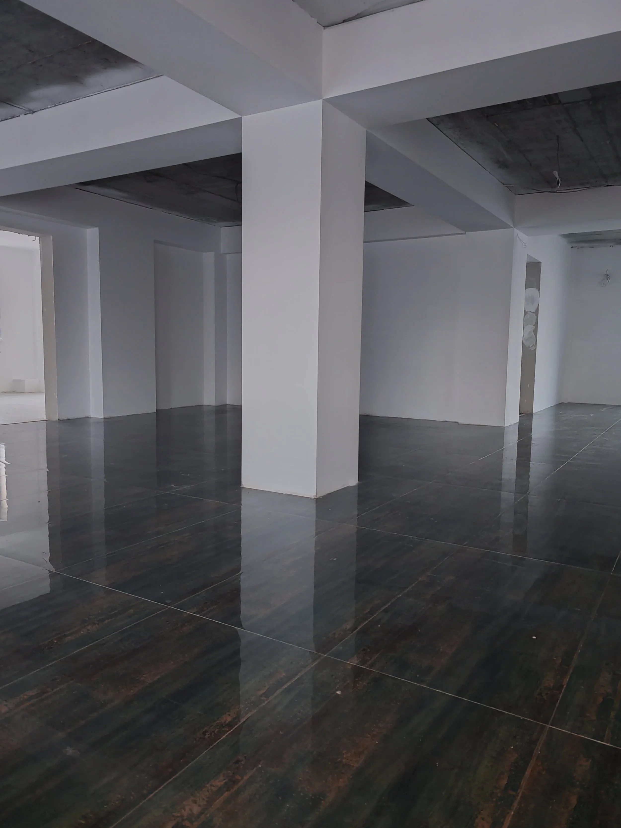 Empty room with white walls, black glossy tiled floor, and exposed ceiling with visible wiring, possibly under construction or renovation.