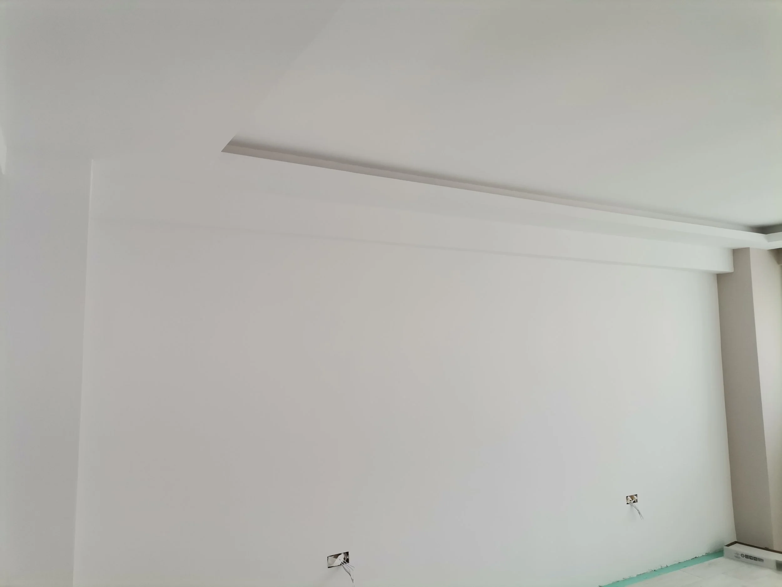 An interior room with white walls and ceiling, with electrical outlets and wiring visible, and a floor covered with green protective material.