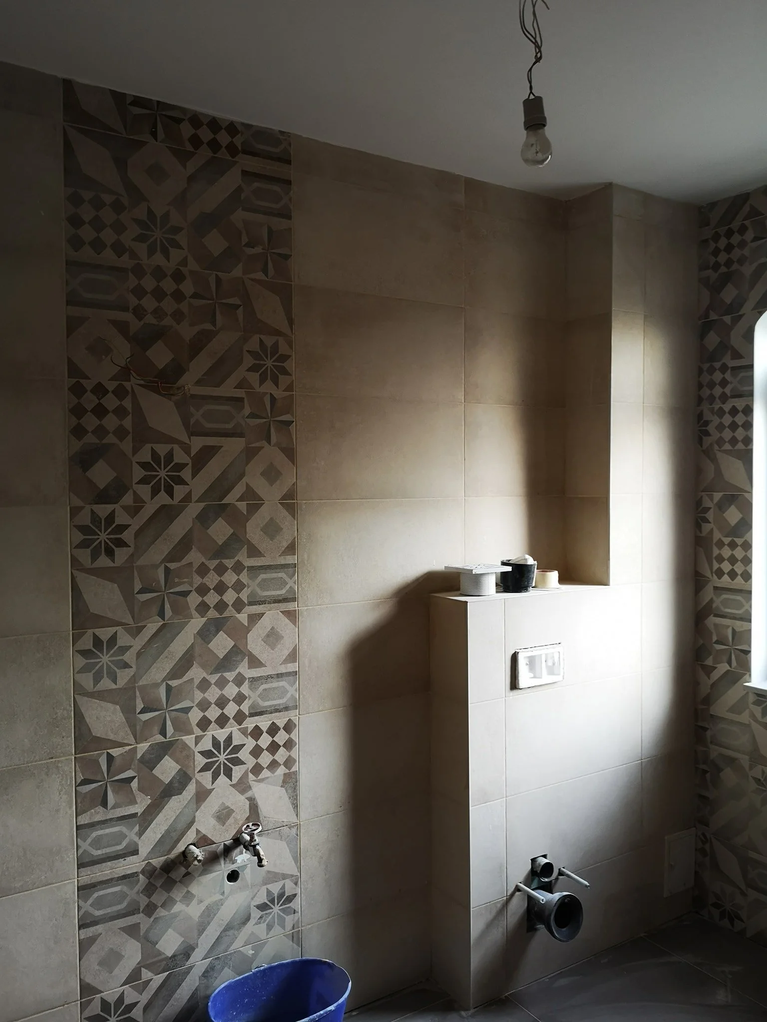 A partially renovated bathroom showing tiled walls, some unconnected plumbing fixtures, a bucket, and construction materials.
