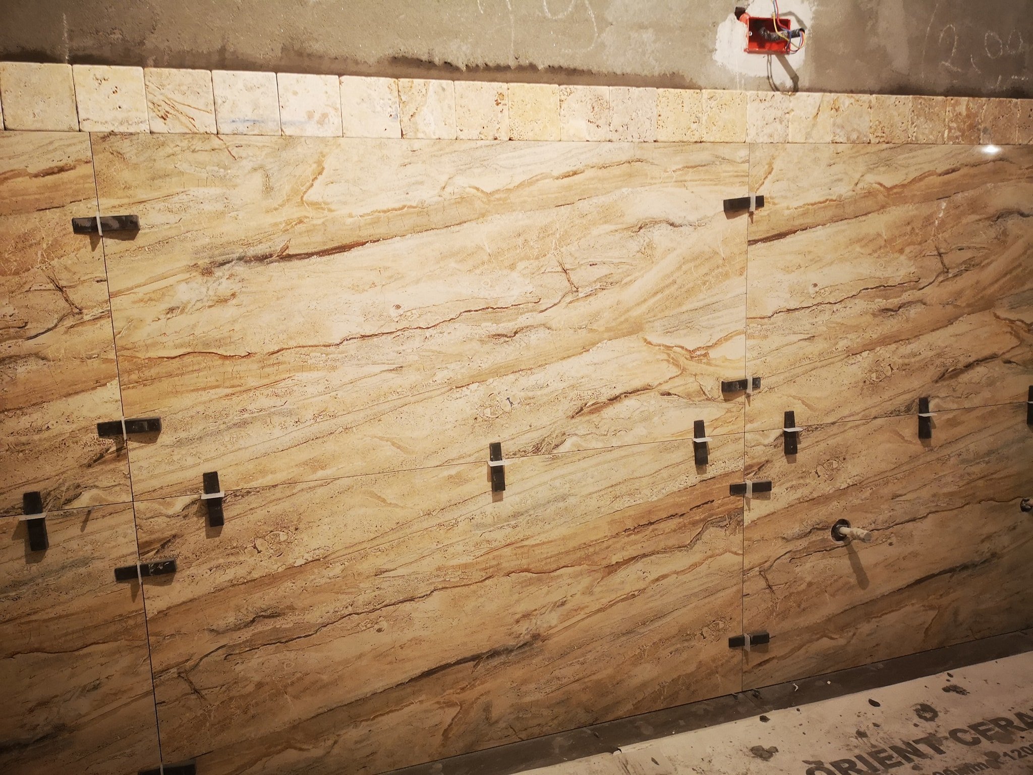 A wall of large, rectangular, natural stone tiles with beige and brown tones, being installed in a construction or renovation site.