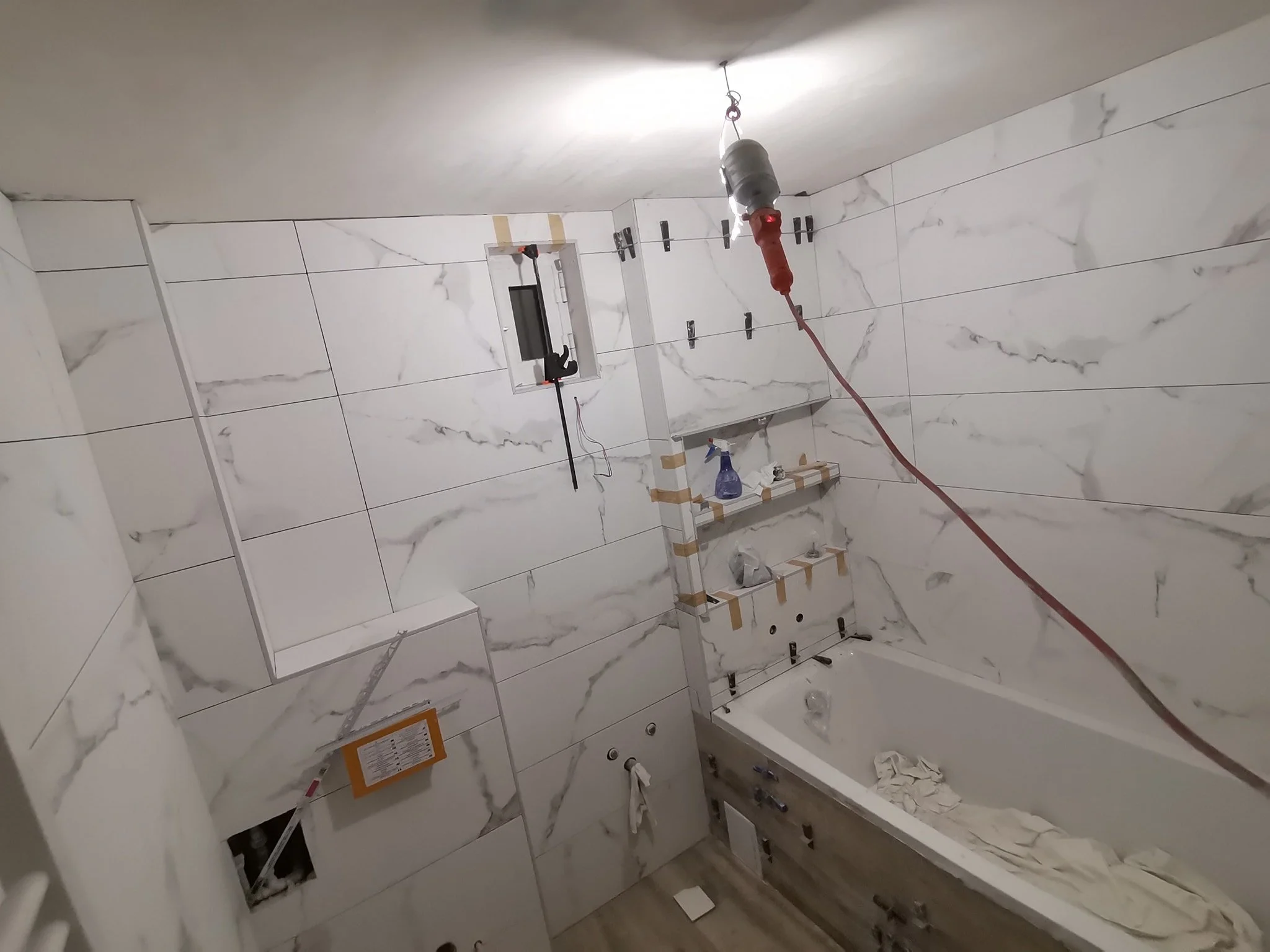 A bathroom under construction with white marble wall tiles, plumbing fixtures, and construction tools and materials scattered around.