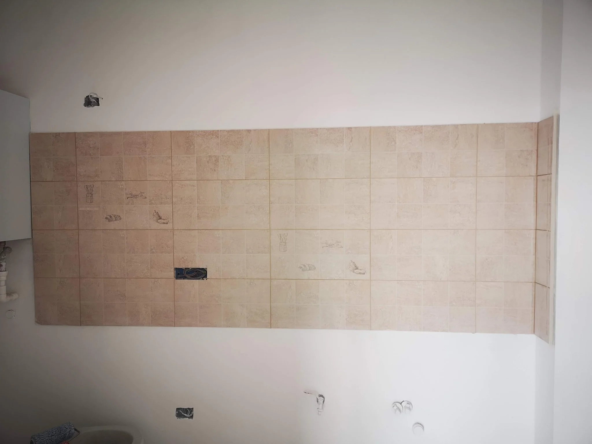 Unfinished room with upper wall painted white, partially tiled lower wall, and electrical outlets and wiring exposed.