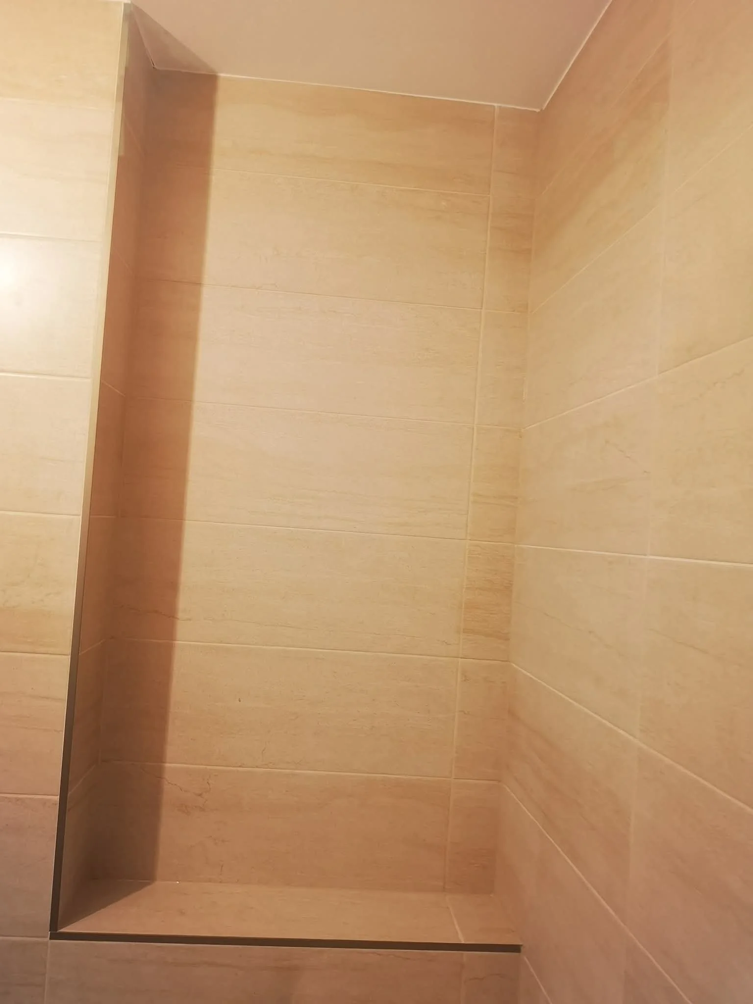 Empty shower with beige tiles and a glass door.