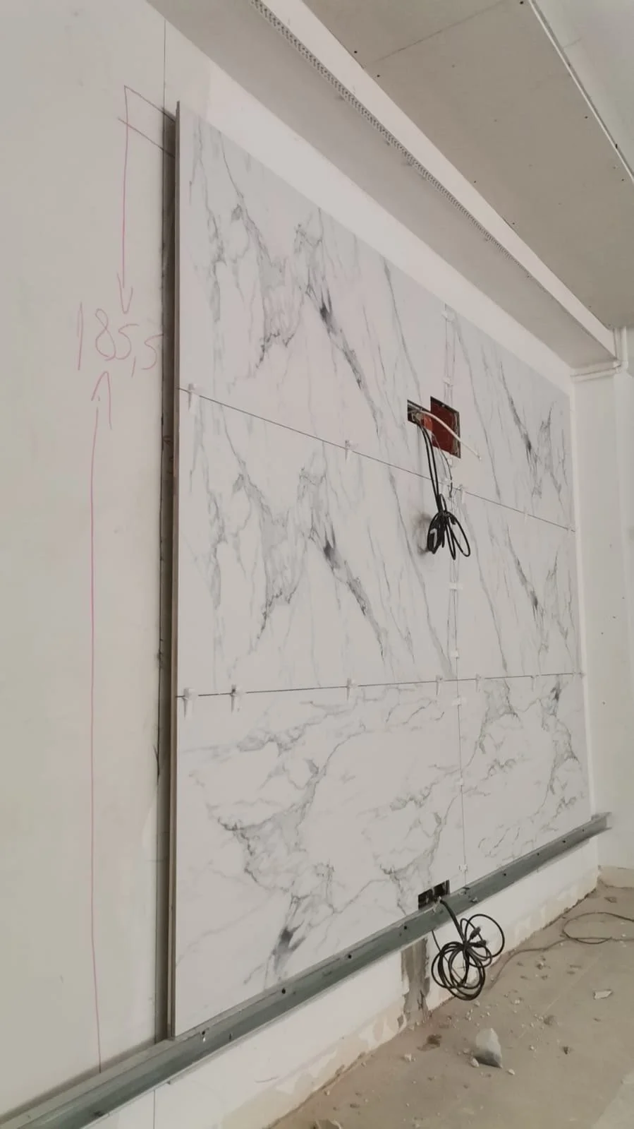 Installing marble tiles on a wall, with markings and wiring for electrical work in progress.