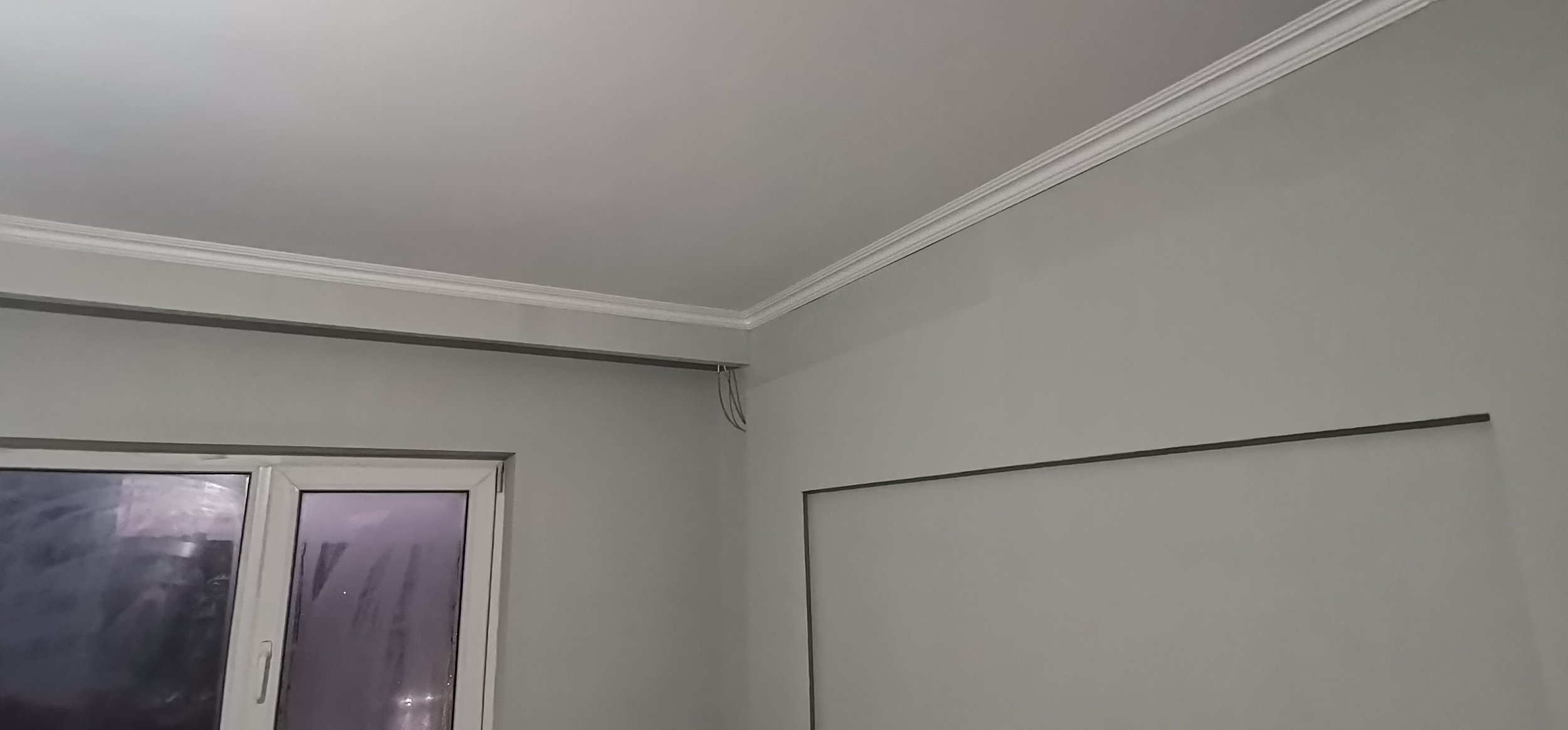 Room interior with ceiling molding, a window, and visible wires near the top corner.