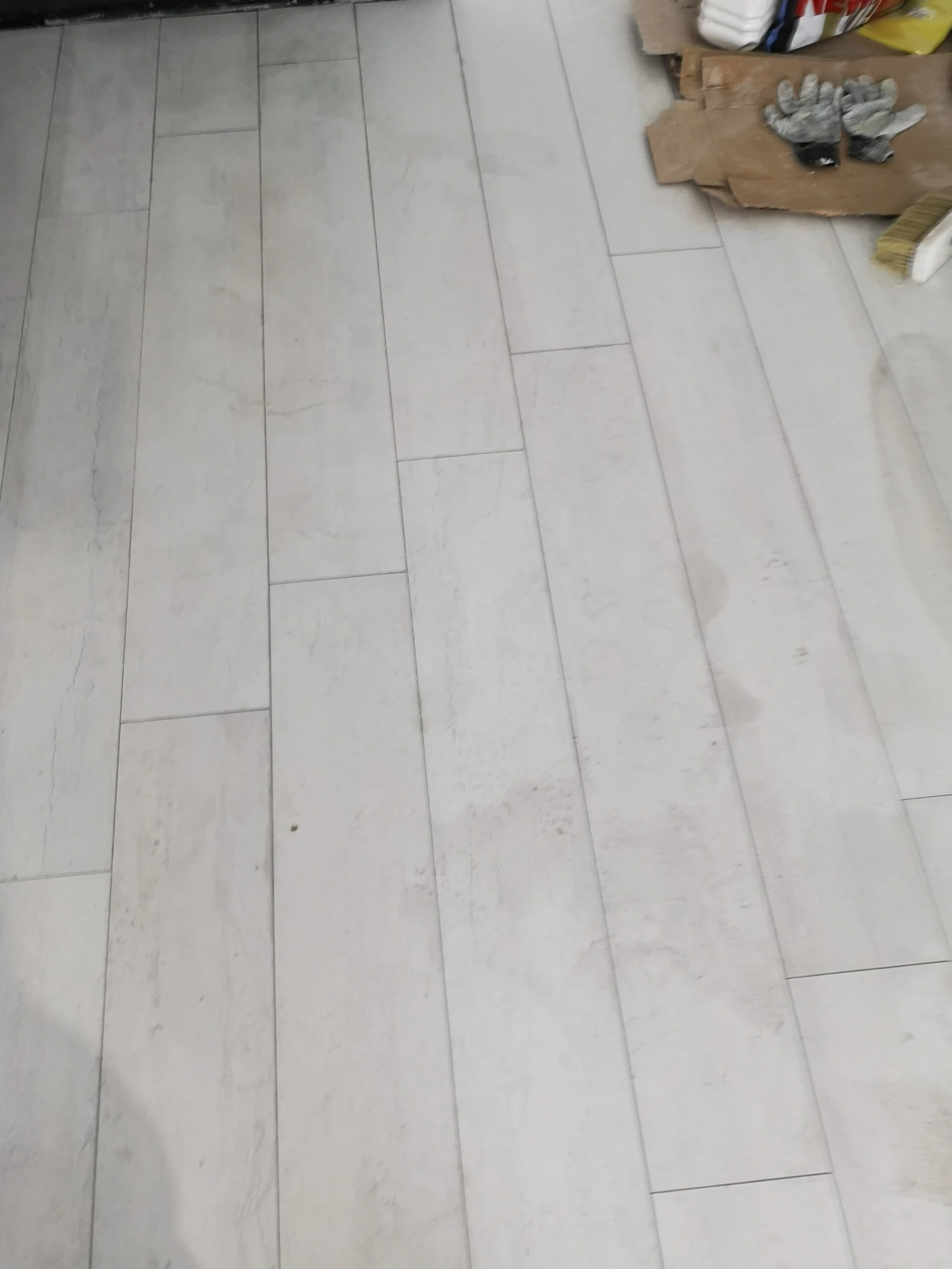 A tiled floor with some construction or cleaning tools, such as gloves and brushes, in the corner.