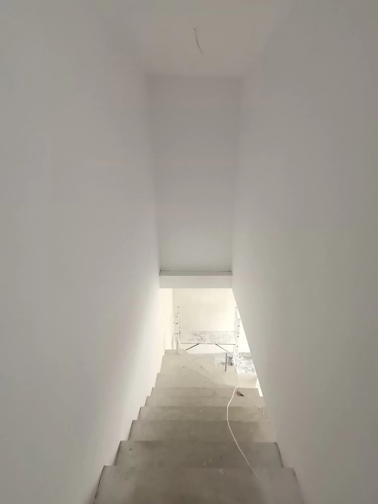 Empty staircase in an unfinished building with white walls and construction materials in the background.