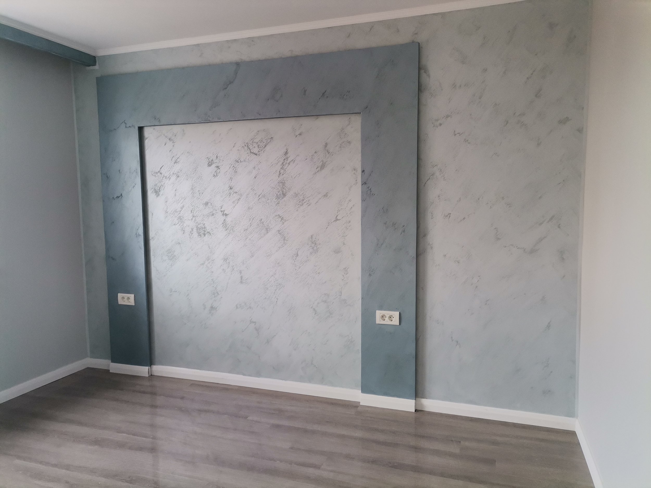 Empty room with gray walls, two electrical outlets, and wood-look flooring