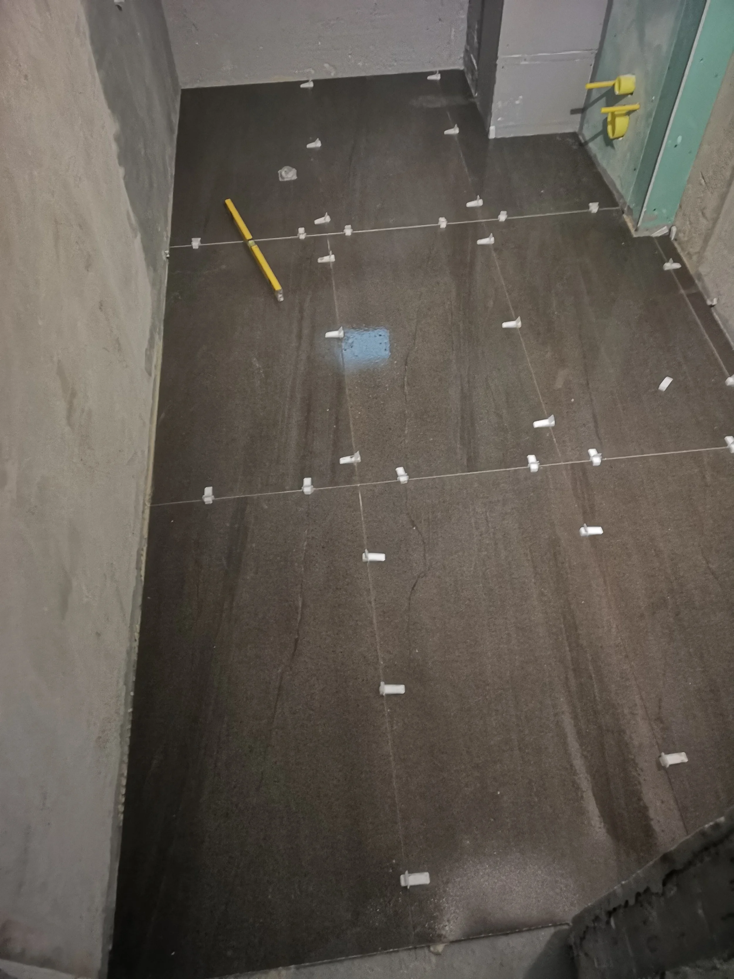 Tile floor with spacers and a level tool in an unfinished room under construction.