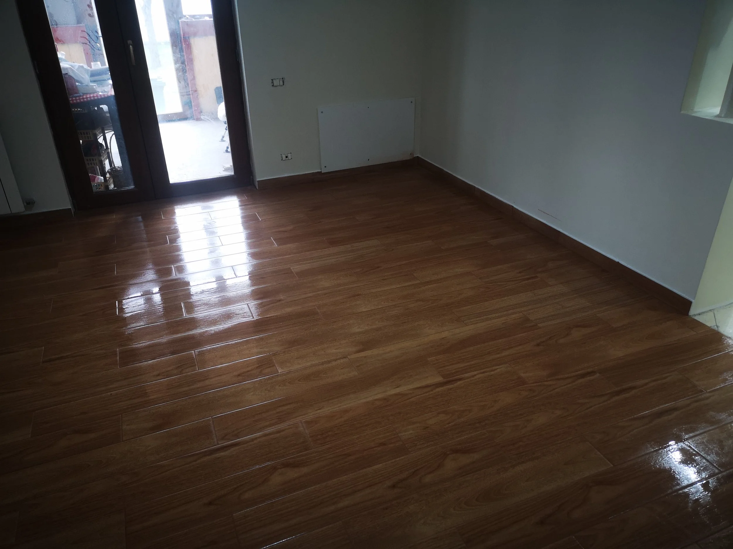 Empty room with wooden flooring, a balcony door on the left, and a small window on the right wall.