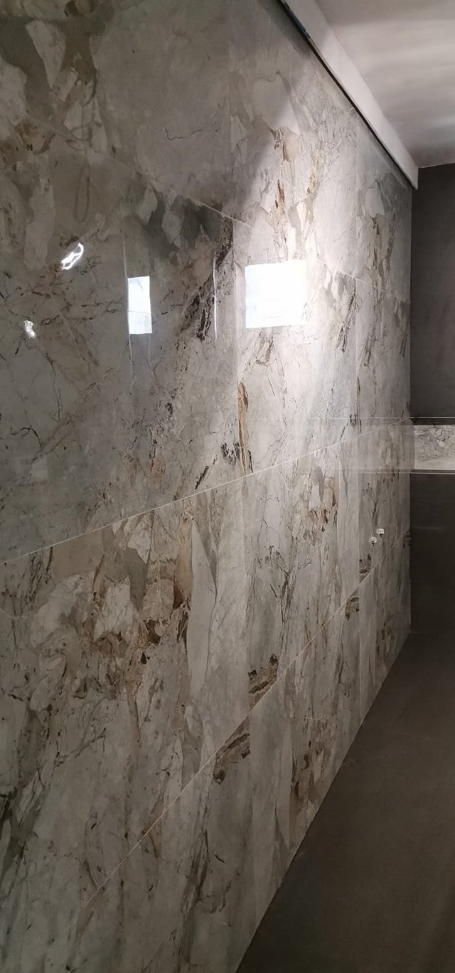 Close-up of a marble or stone tile wall with two small windows and gray concrete floor.