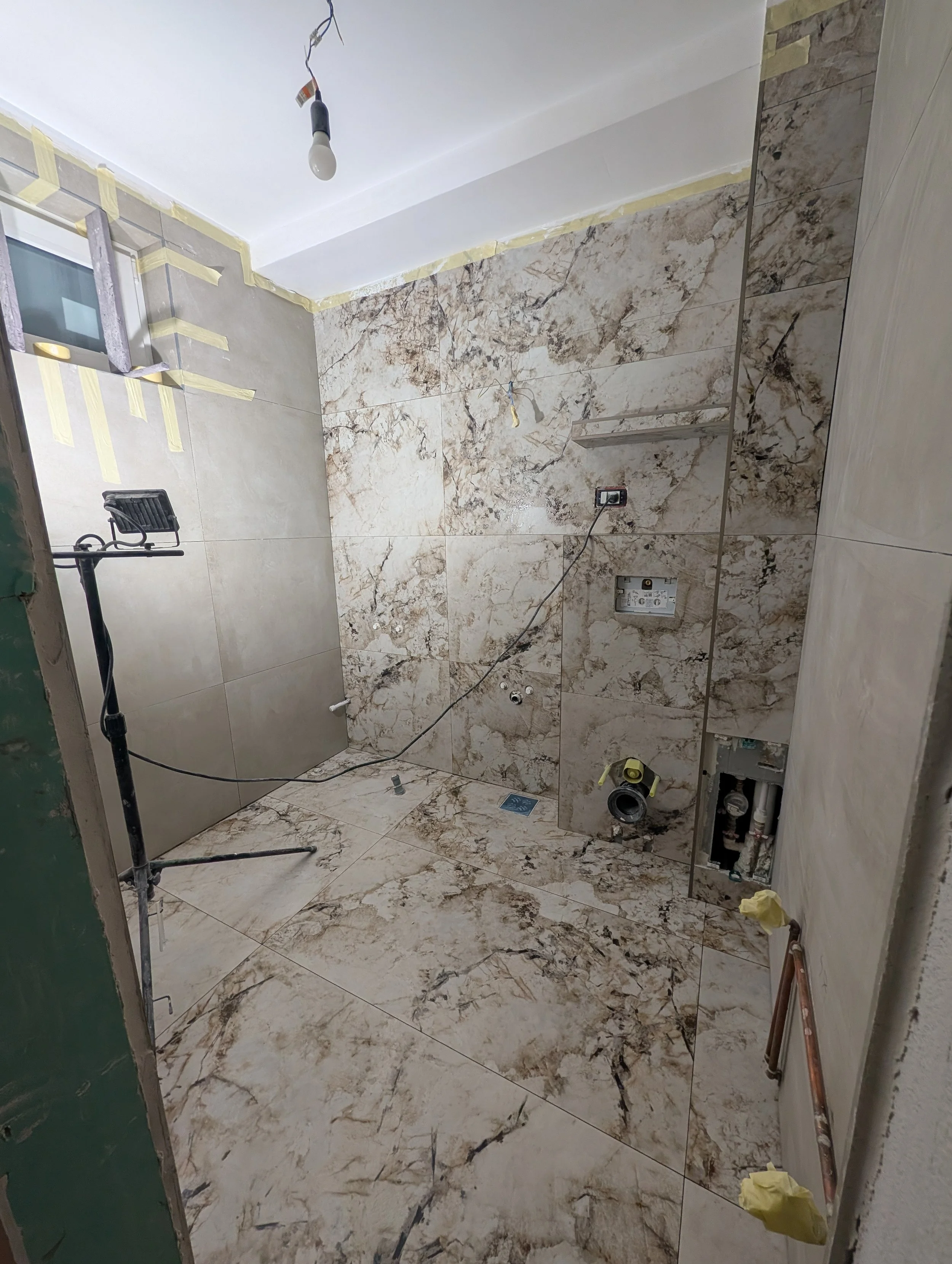 Unfinished bathroom with marble tiles, exposed wiring, plumbing, and construction materials.