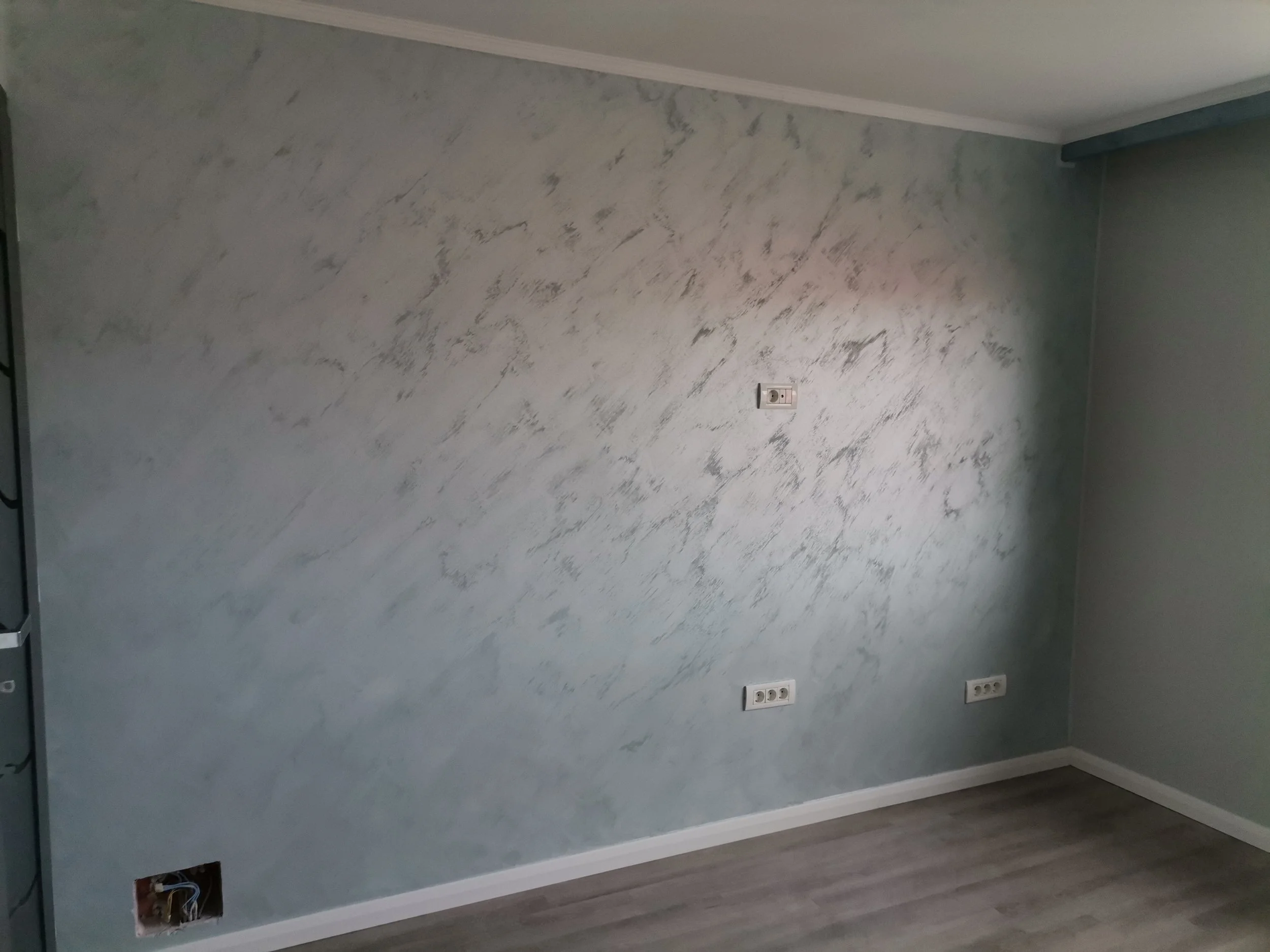 Empty room with gray textured wall, multiple electrical outlets, and a small window in the corner.