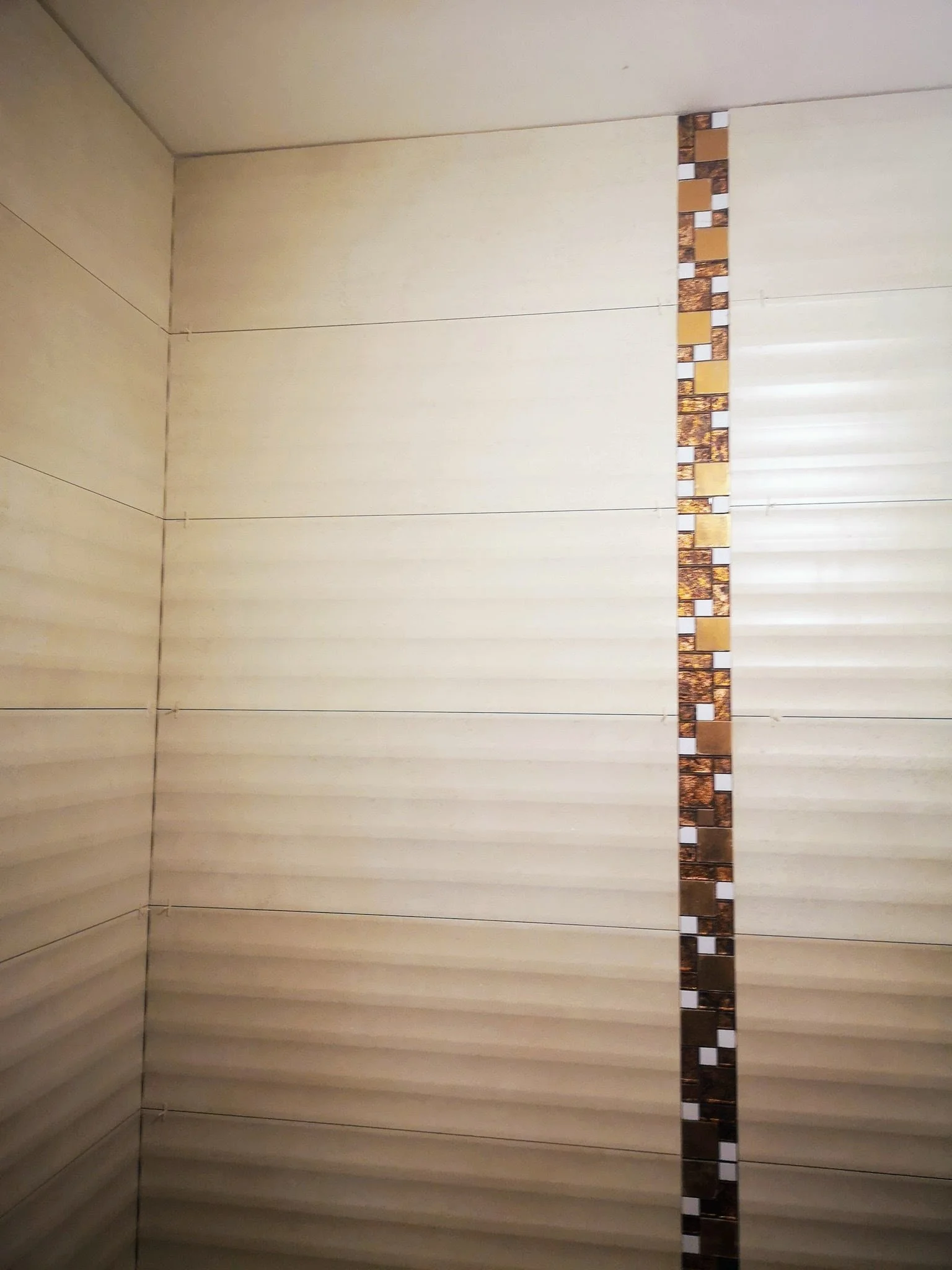 Close-up view of a ceiling with decorative tiles along the edge. The ceiling appears to be made of cream-colored panels with a textured finish. The decorative tiles are arranged in a vertical strip and consist of small rectangular pieces in shades of