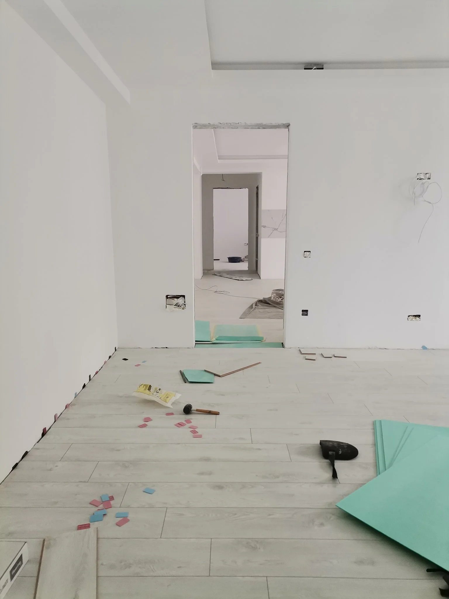 Interior of a room under construction with white walls, unfinished door frame, scattered insulation, tools, and construction debris on the floor.